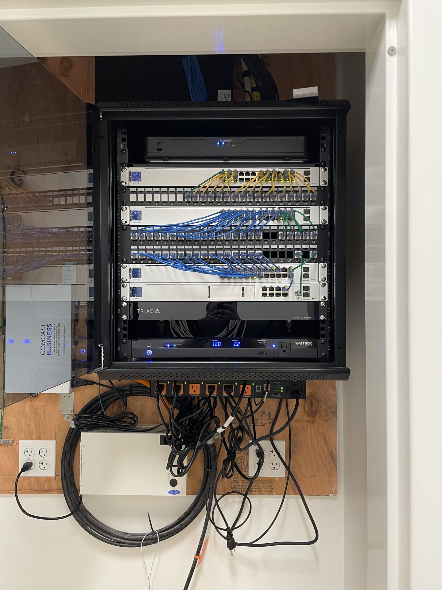 Wall-mounted network rack with labeled Cat6 patch panels, PoE switches, recorder and power conditioning for an Orlando school campus