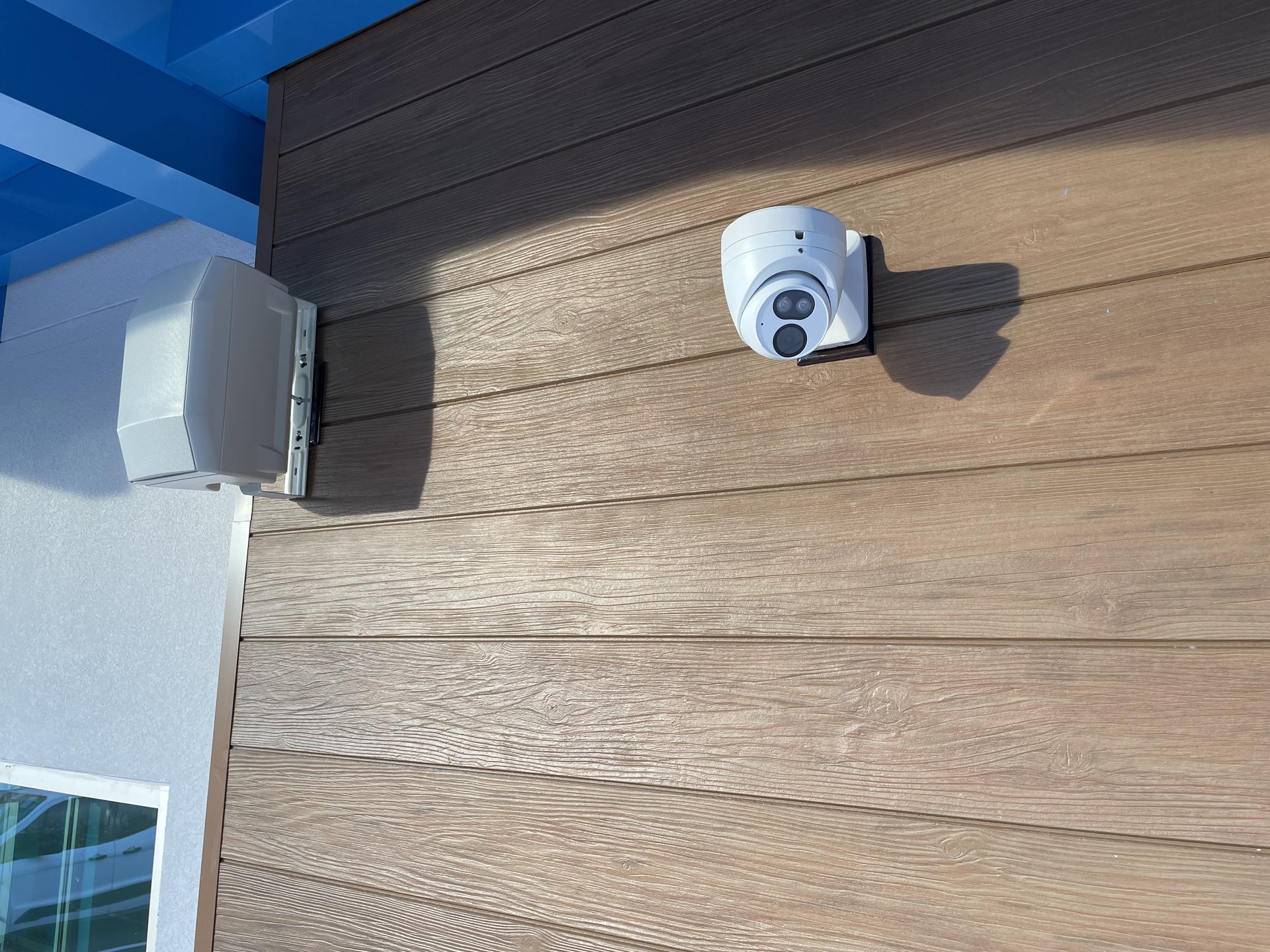 Close-up of an exterior dome security camera and speaker cleanly mounted to the wood-look facade of an Orlando school
