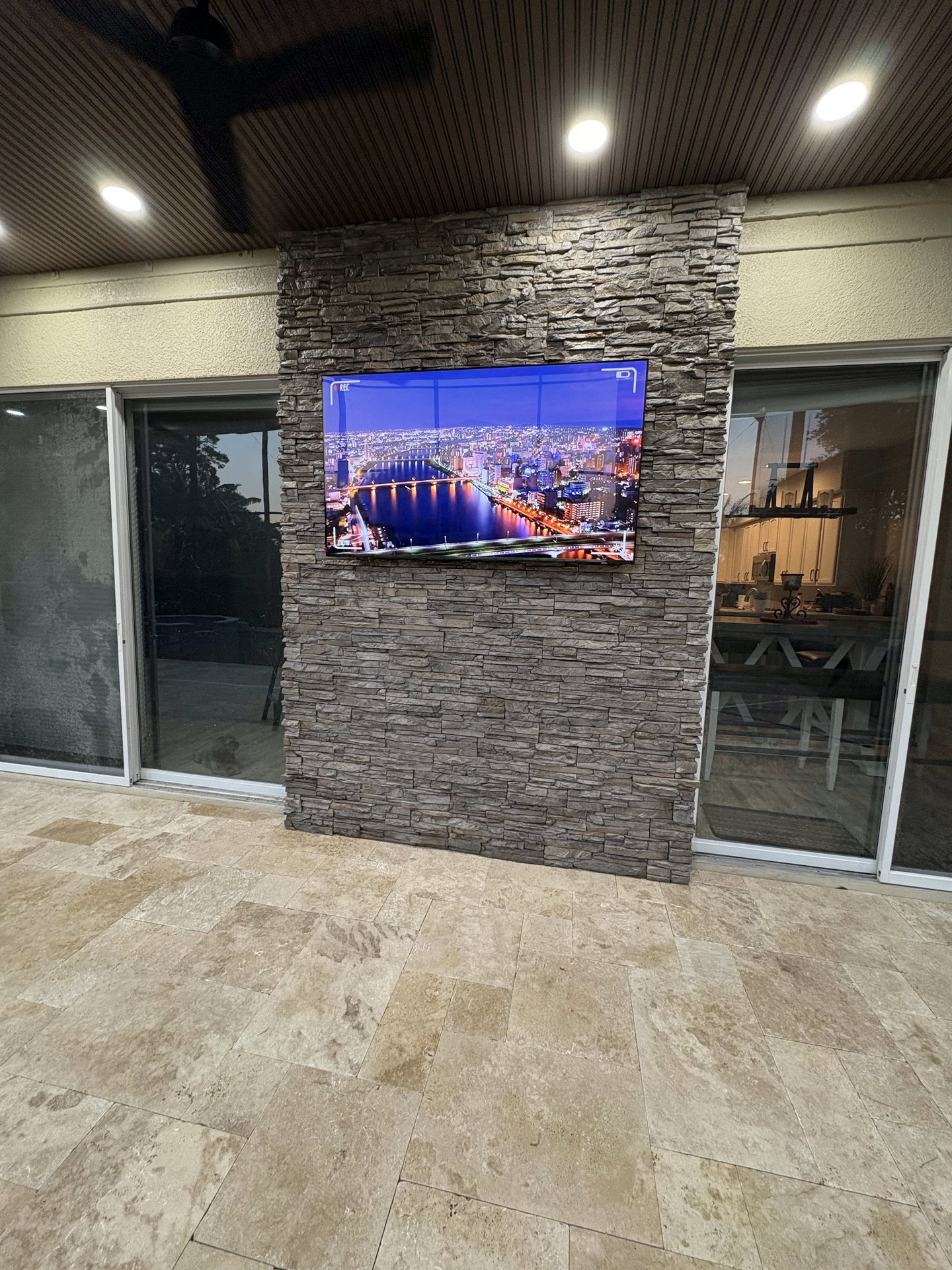 Outdoor display mounted to a stacked stone feature wall on the covered patio