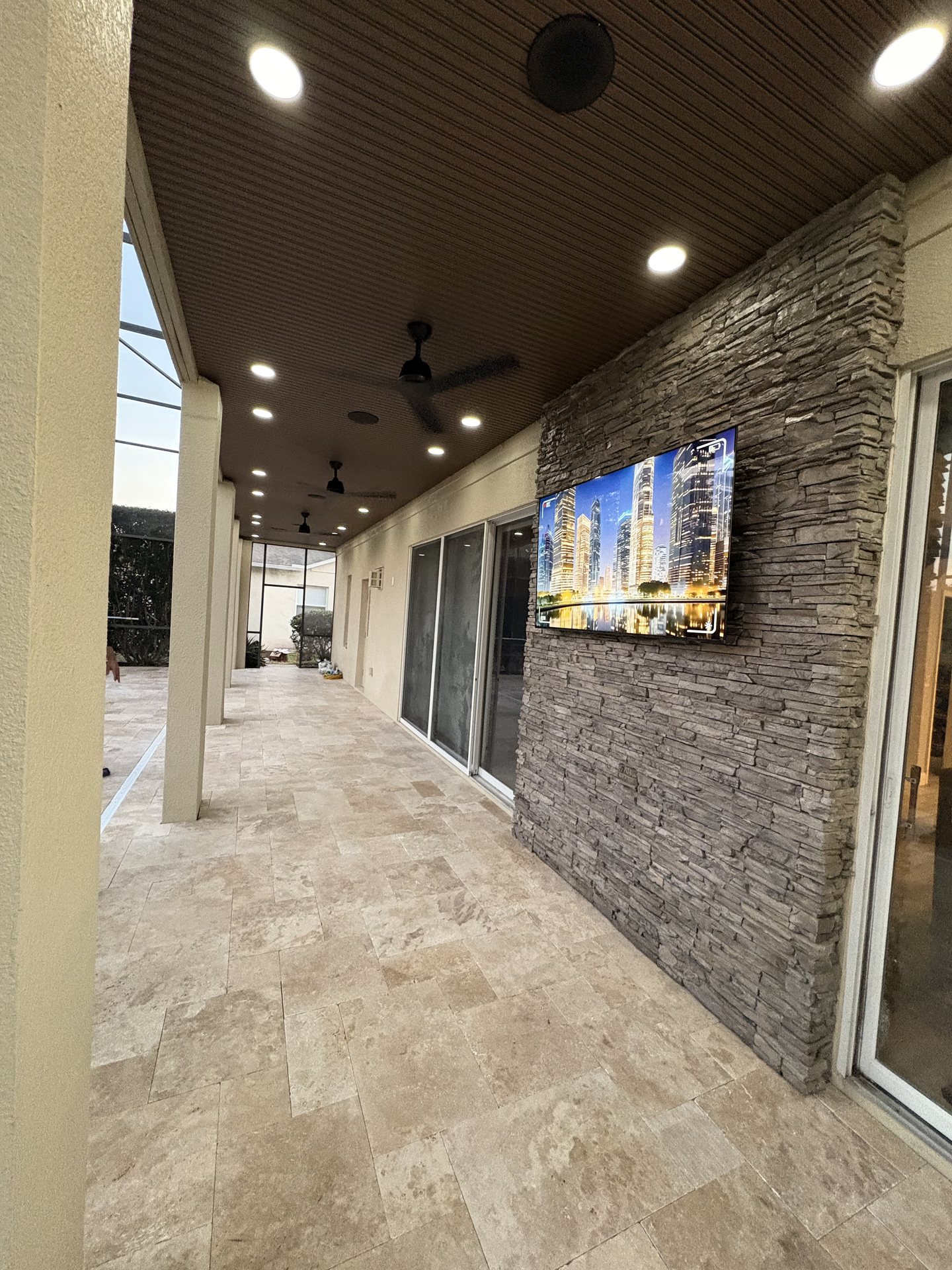 Patio entertainment area with mounted outdoor TV, ceiling fans and integrated lighting