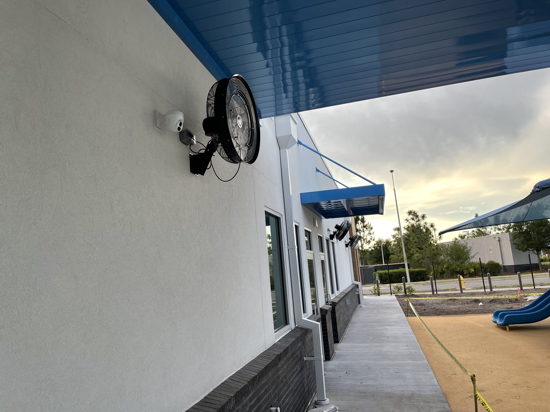 Exterior walkway of an Orlando school with a security camera and canopy speakers covering the entry and play area