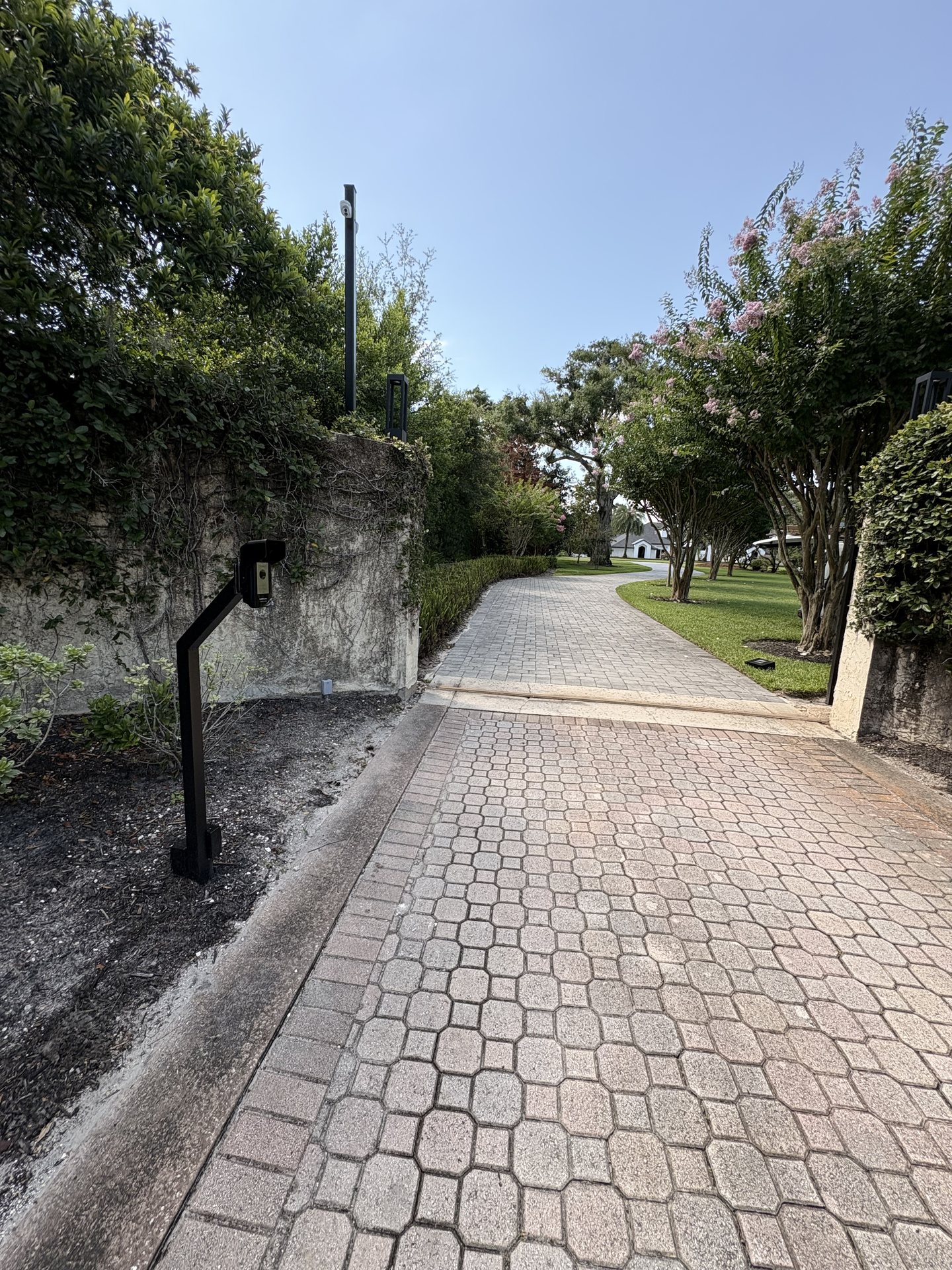 Low-profile intercom pedestal set beside the paver driveway entry with buried low-voltage cabling